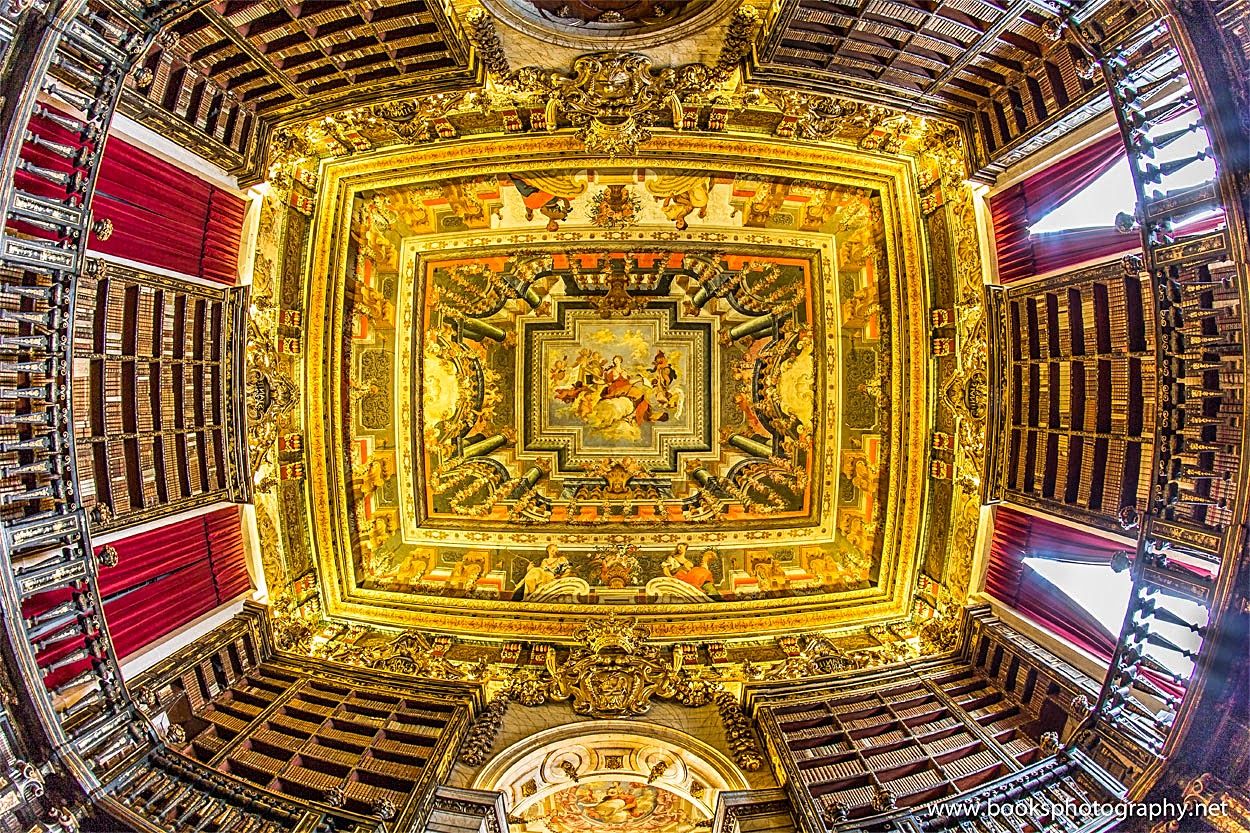 Interior of the Joanina Library in Coimbra, Portugal, featuring its stunning Baroque design, elaborately decorated bookshelves, and ornate reading tables.