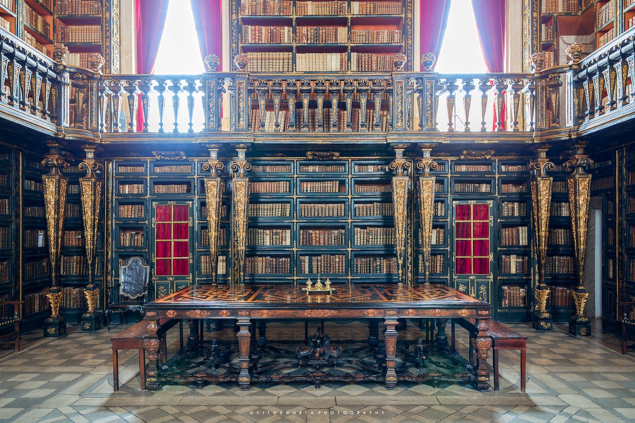 Interior of the Joanina Library in Coimbra, Portugal, featuring its stunning Baroque design, elaborately decorated bookshelves, and ornate reading tables.