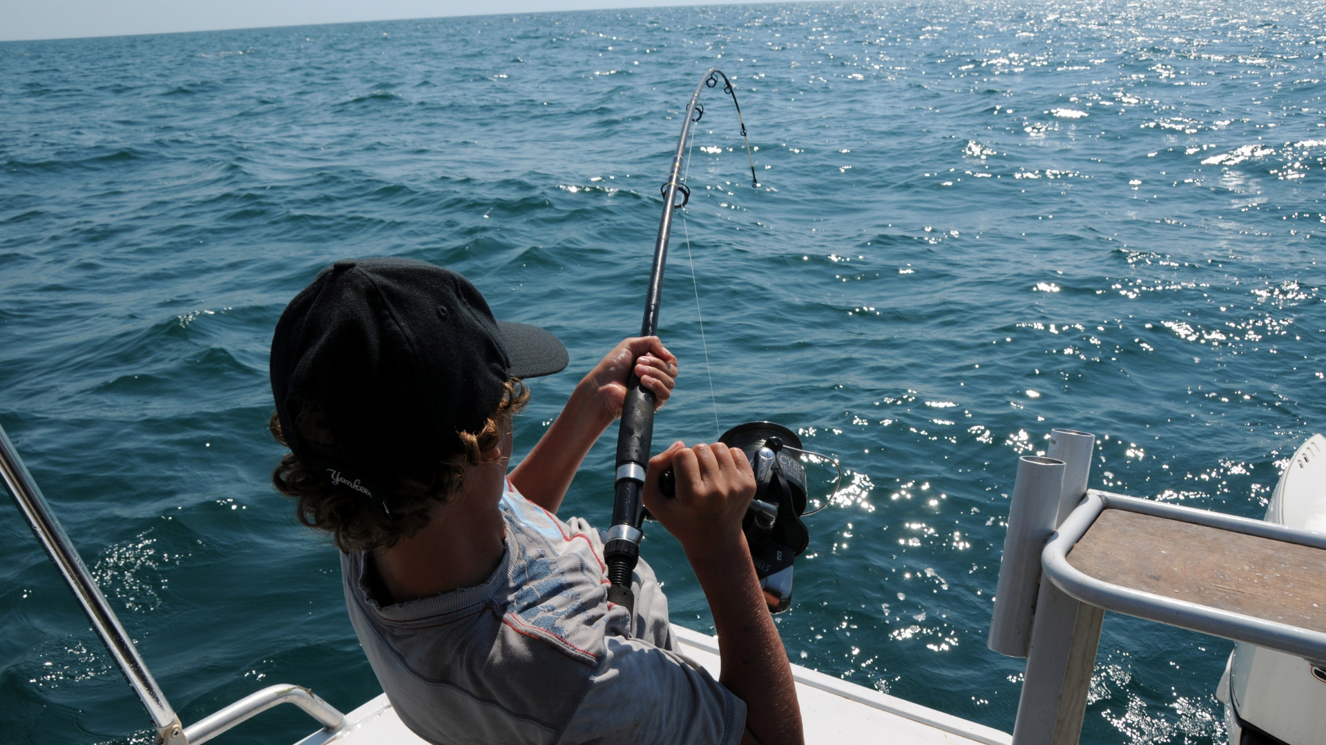 Big Game Fishing: Anglers aboard a fishing boat off Madeira’s coast, reeling in a blue marlin under clear skies.