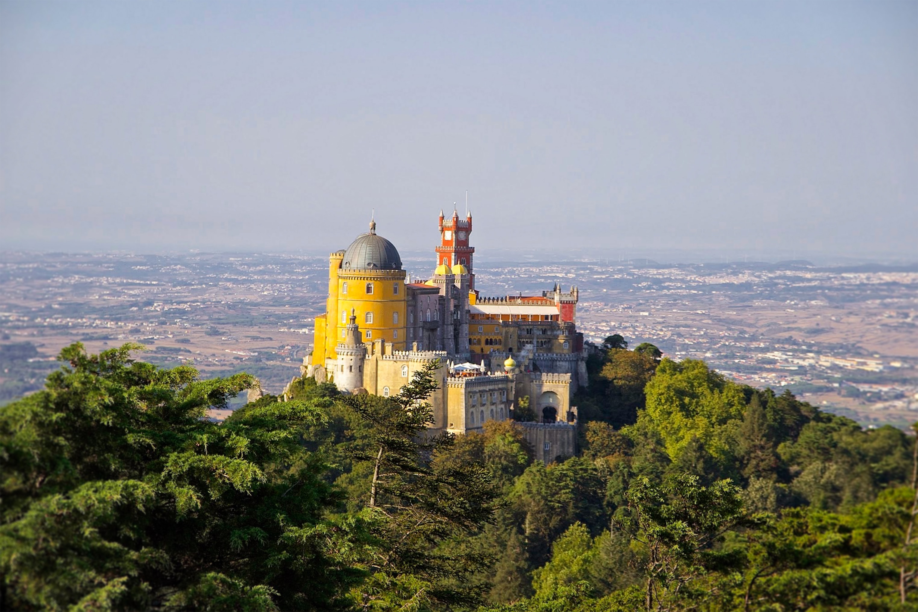 Exterior view of Sintra Palace (Palácio Nacional de Sintra) in Portugal, characterized by its distinctive blend of architectural styles, including Gothic, Moorish, and Manueline influences, set against a backdrop of lush greenery.