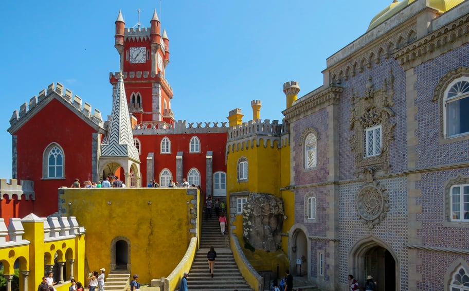 Exterior view of Sintra Palace (Palácio Nacional de Sintra) in Portugal, characterized by its distinctive blend of architectural styles, including Gothic, Moorish, and Manueline influences, set against a backdrop of lush greenery.
