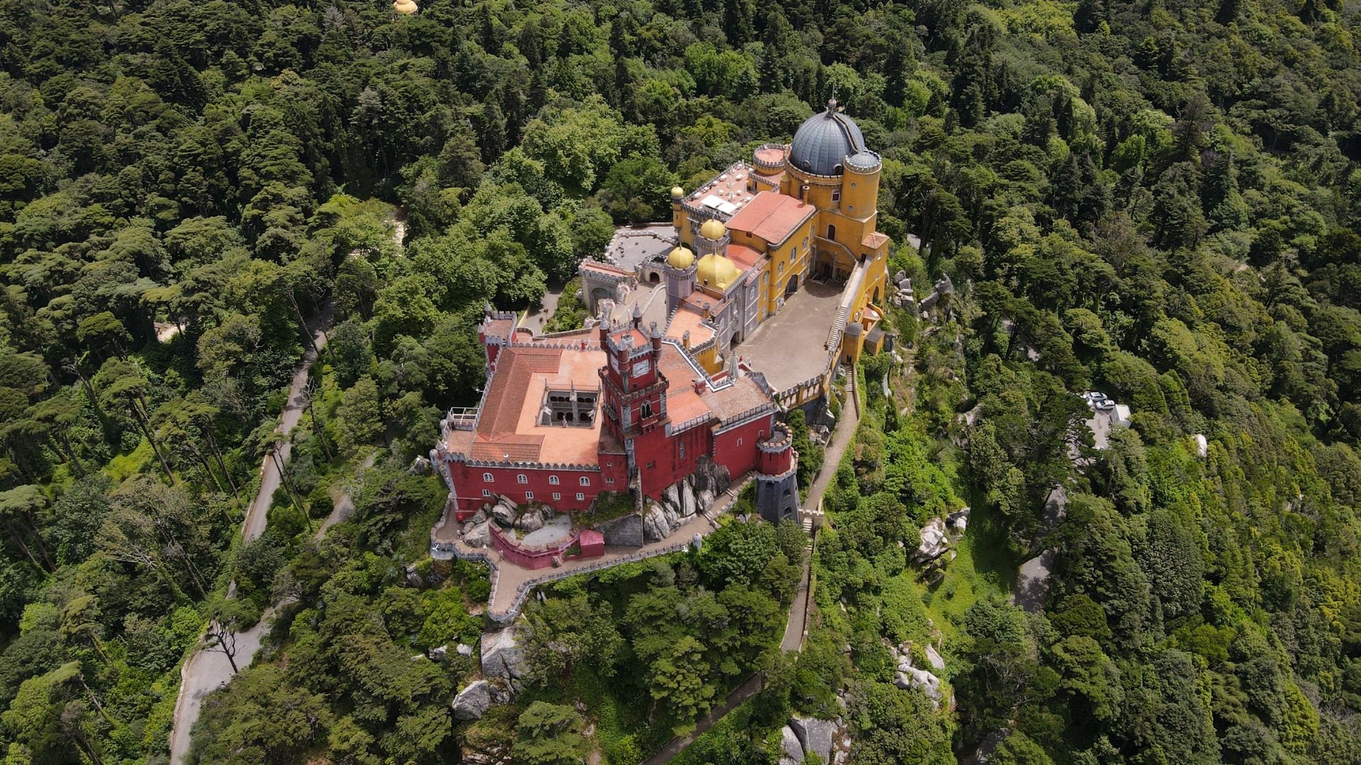 Exterior view of Sintra Palace (Palácio Nacional de Sintra) in Portugal, characterized by its distinctive blend of architectural styles, including Gothic, Moorish, and Manueline influences, set against a backdrop of lush greenery.